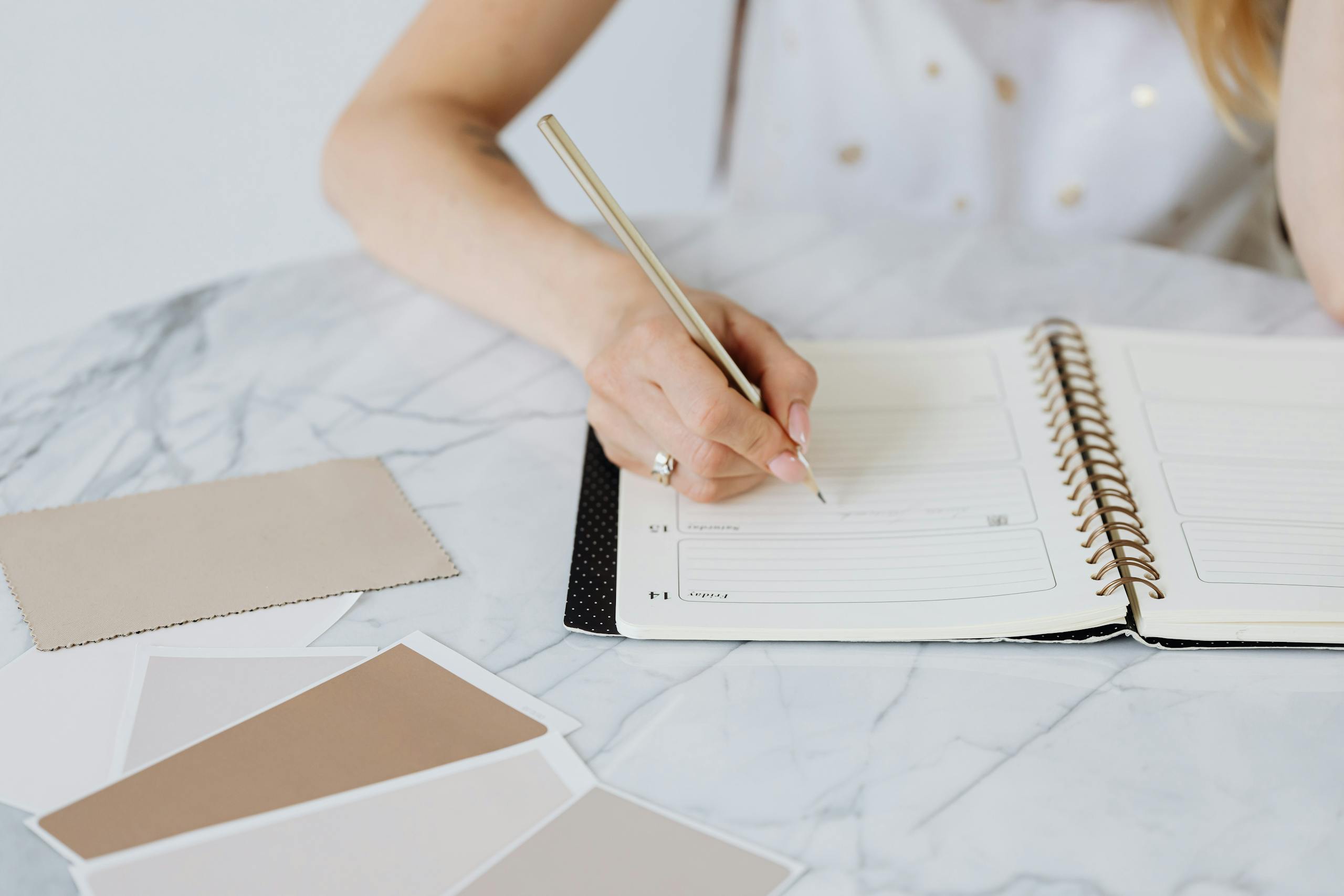 Woman with Writing in a Calendar and Beige Colour Samples on White Table